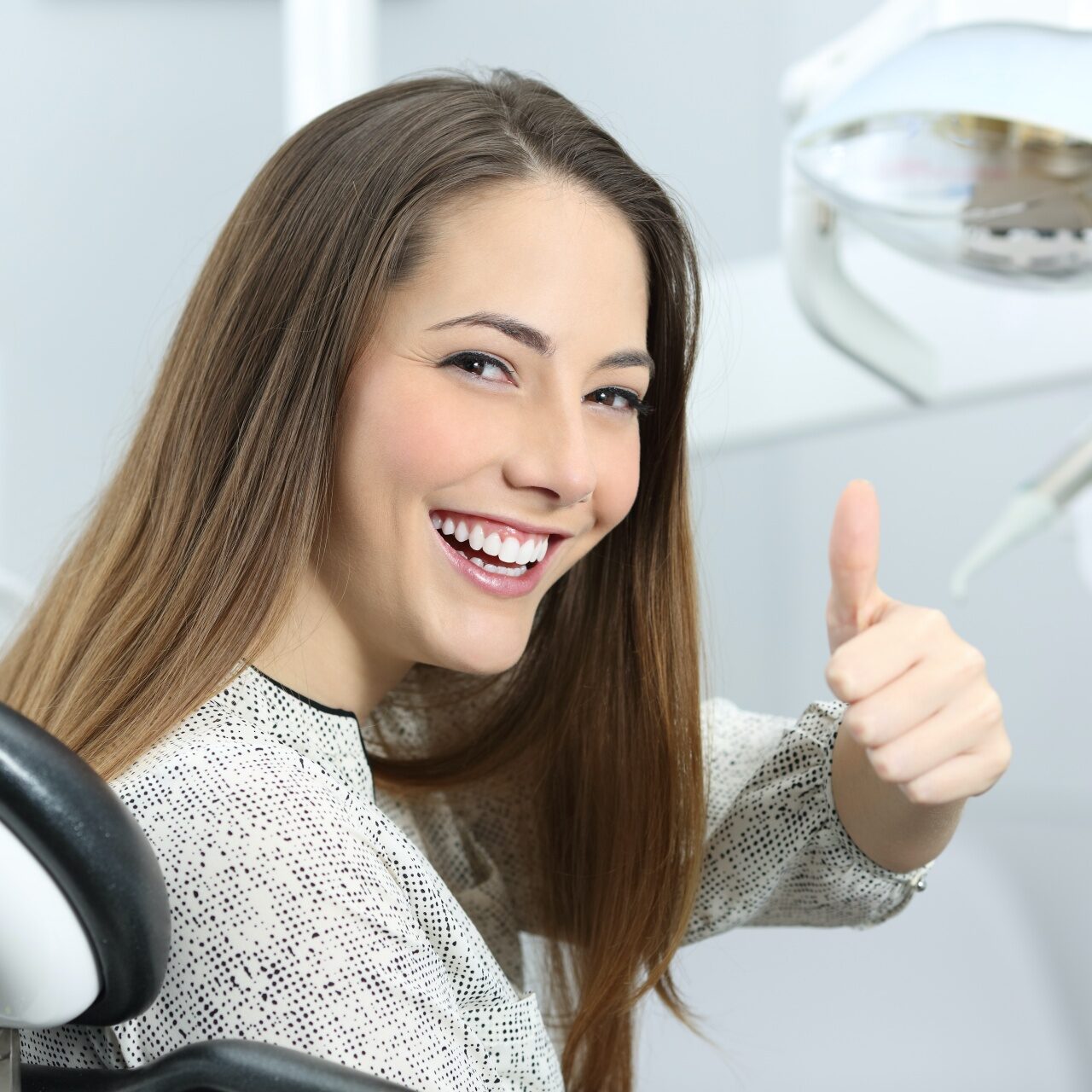 shutterstock_592789712 Woman smiling and giving a thumbs up in a dentist chair